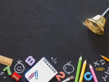 Bell and school supplies on blackboard