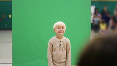A cute young child is smiling as they get their school picture taken in front of a green screen.