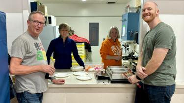 4 Adults standing at a counter who support the community breakfast program at the school